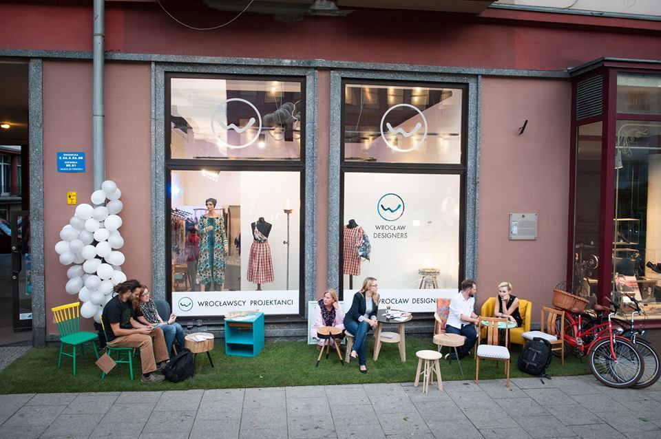 Wrocławska ulica: przed sklepem Wrocławscy Projektanci, przy stolikach siedzą młodzi, rozmawiający ze sobą ludzie