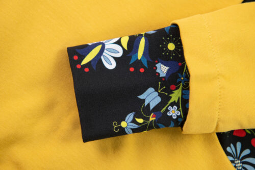 Mankiet żółtej bluzy wykończony tkaniną z kolorowym folkowym wzorem na czarnym tle